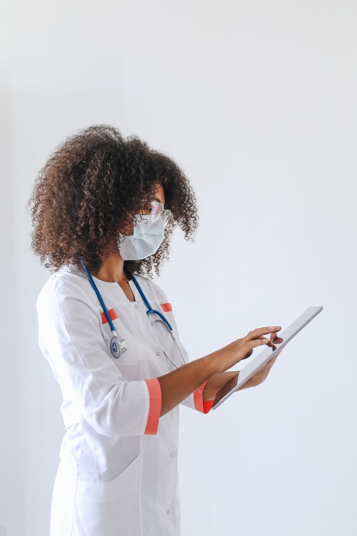 The Art of Drawing Readers In: Your attractive post title goes here A female doctor in a white coat and face mask using a tablet for data entry in a medical setting.
