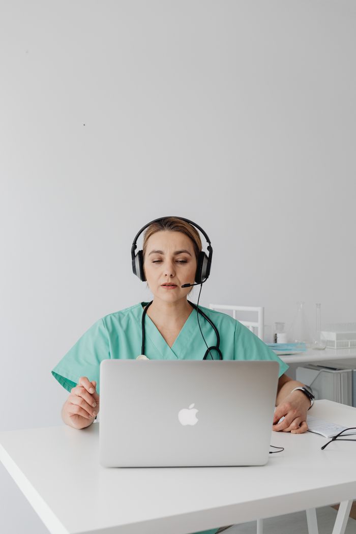A female doctor in green scrubs conducts an online consultation using a laptop.